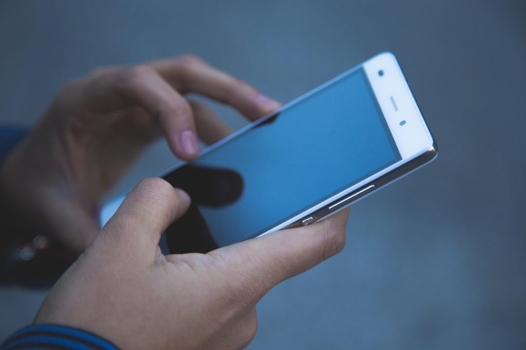 Hands holding a smartphone mid-tap against a grey background, standing in for the vertical feed where TikTok's automated targeting decides who sees an ad