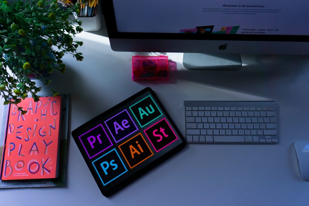 Designer's desk with a hand-lettered graphic design playbook and Adobe app icons on a tablet, illustrating who controls the words on ad creative