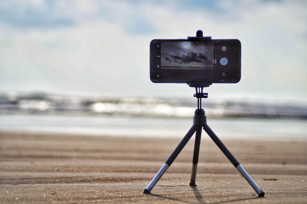 Smartphone mounted horizontally on a small tripod filming a shoreline, illustrating horizontal footage being reframed for vertical ad placements
