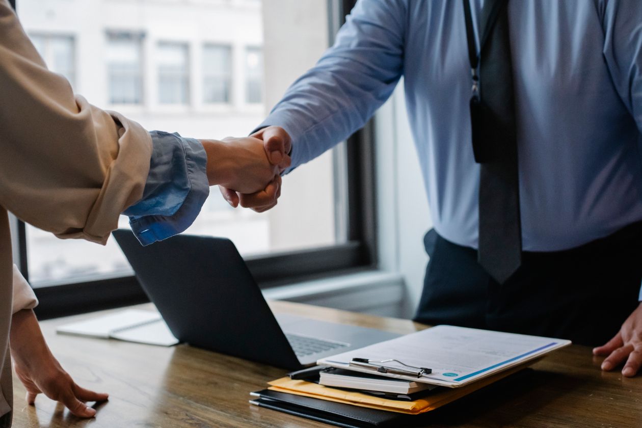 Business owner shaking hands with a returning client across a desk with a laptop and clipboard, illustrating new versus existing customer classification