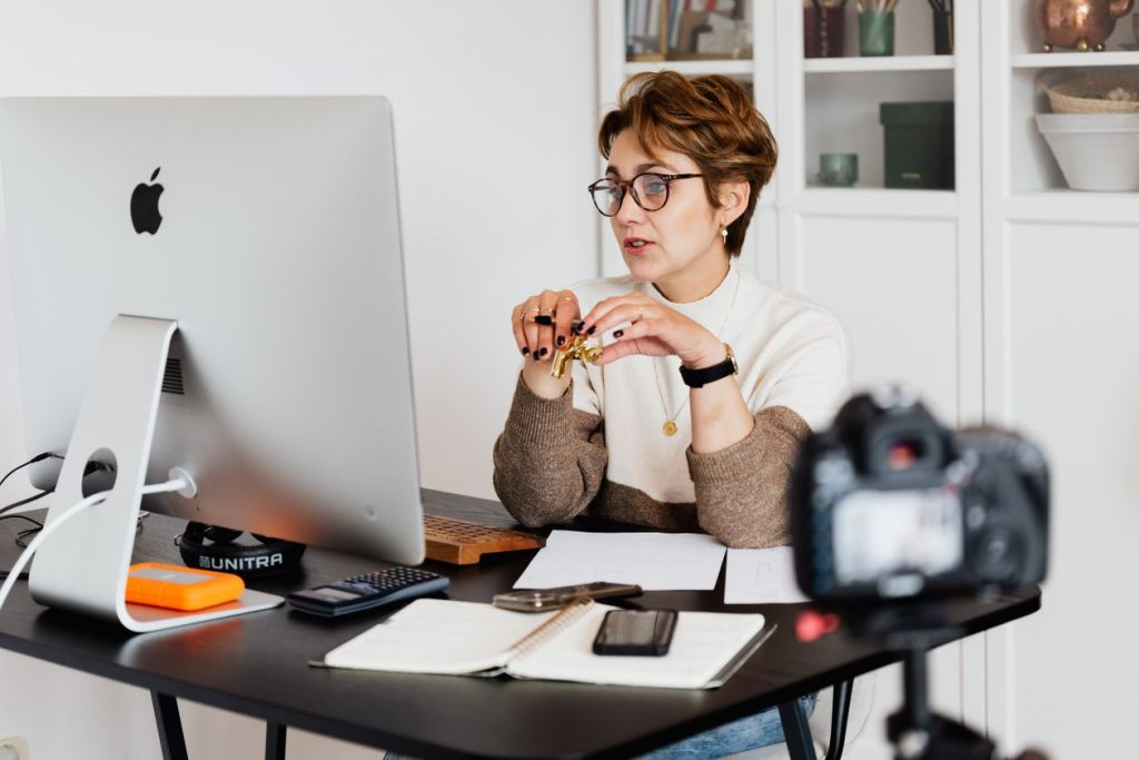 Small-business owner working at a desk beside a camera on a tripod, illustrating the still-image assets a two-person team can shoot for YouTube ads