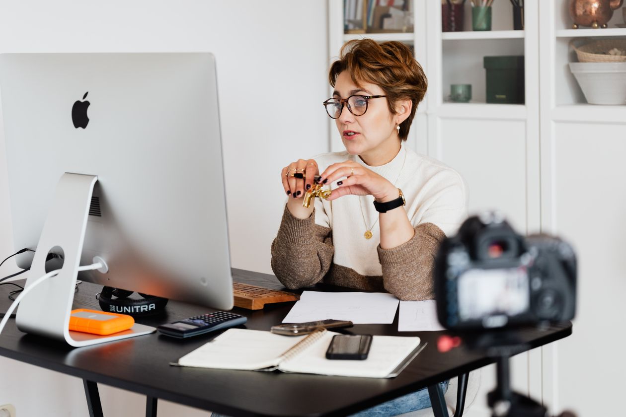 Small-business owner working at a desk beside a camera on a tripod, illustrating the still-image assets a two-person team can shoot for YouTube ads