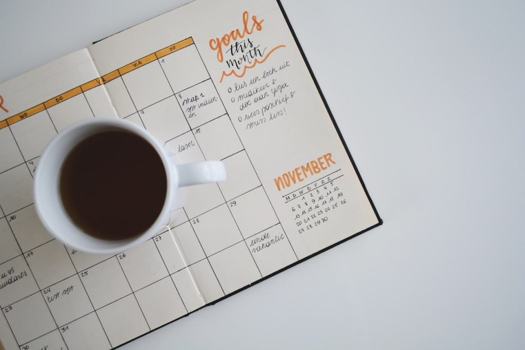 Open monthly planner headed "goals this month" with a cup of coffee resting on the grid, illustrating the September migration window advertisers must date themselves