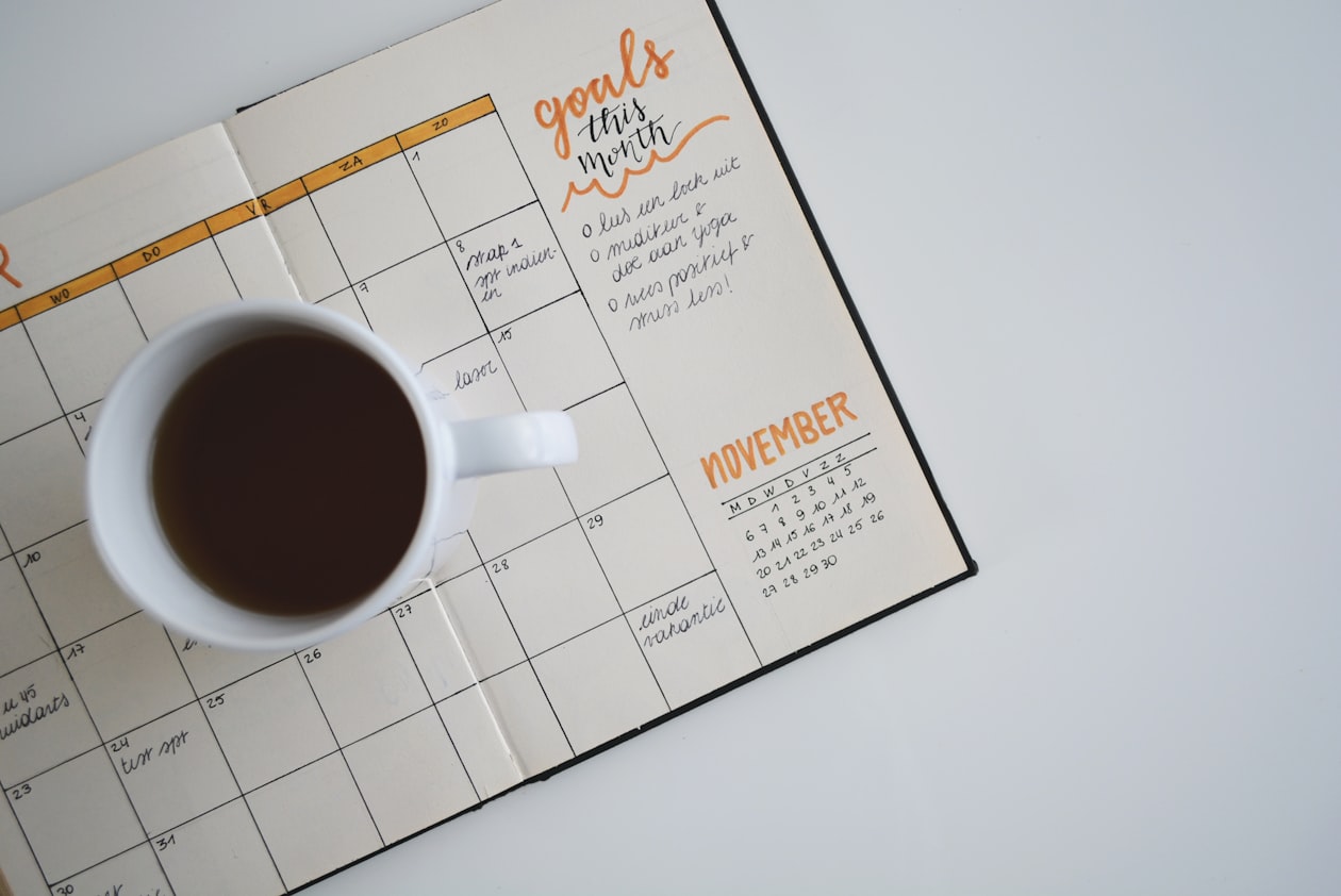 Open monthly planner headed "goals this month" with a cup of coffee resting on the grid, illustrating the September migration window advertisers must date themselves