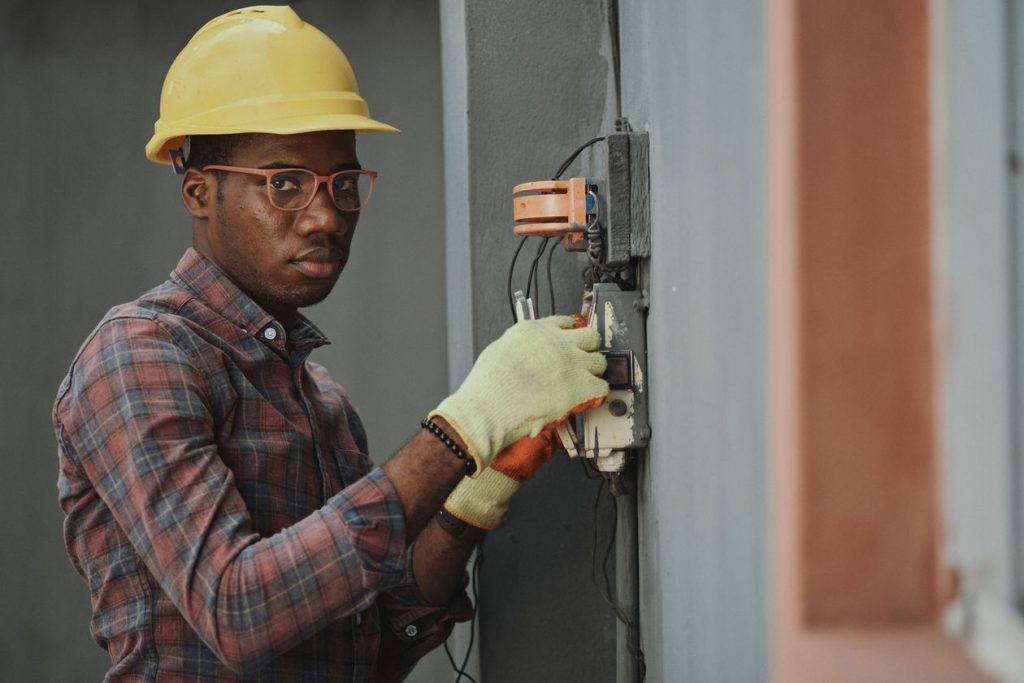 Electrician in a hard hat wiring an outdoor junction box with both hands occupied, illustrating why Local Services Ads calls go unanswered