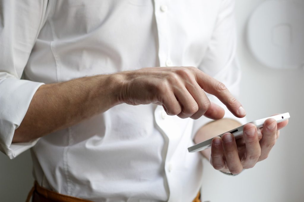 Close-up of a person tapping a smartphone screen with both hands, illustrating the pre-query moment Apple Maps now sells to advertisers