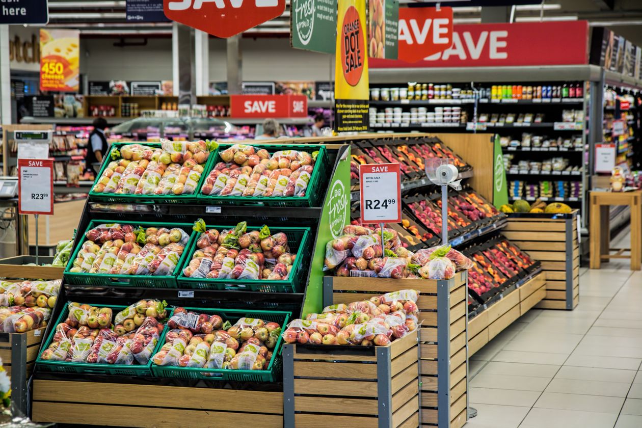 Supermarket produce aisle lined with printed shelf price labels and promotional signs, illustrating how a product title functions as the label a shopper reads