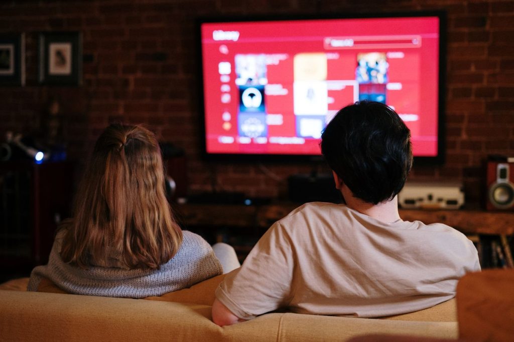 Two people on a couch watching a video app menu on a living-room TV, the kind of playback start YouTube now counts as a public view