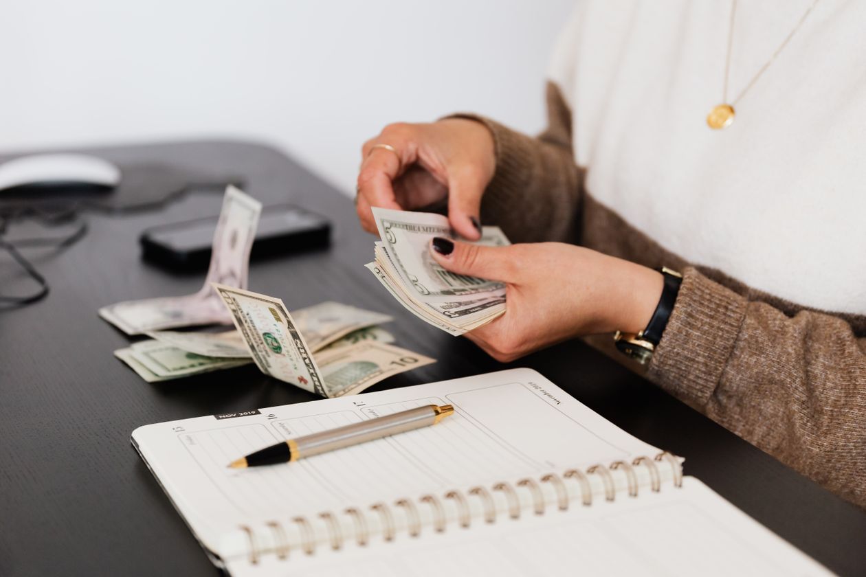 Person counting cash at a desk beside an open notebook and pen, illustrating a small advertiser reconciling ad spend against a promised promotional credit