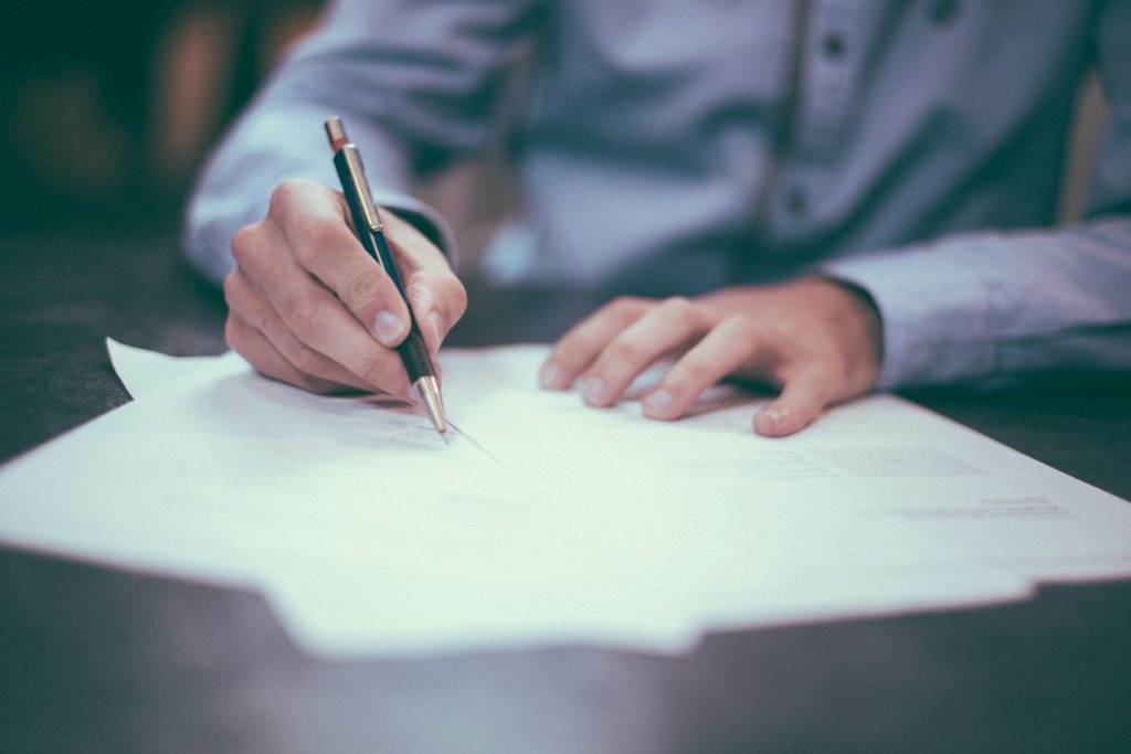 Hand marking up a printed report with a pen at a desk, illustrating the manual verification an AI-written performance summary still requires