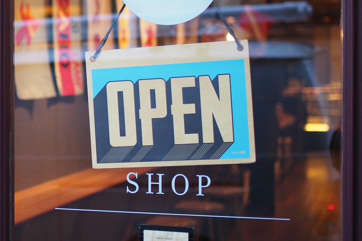 Hand-lettered OPEN sign hanging in a small shop window, illustrating how storefront-style offers now travel from a website into Google Search ads