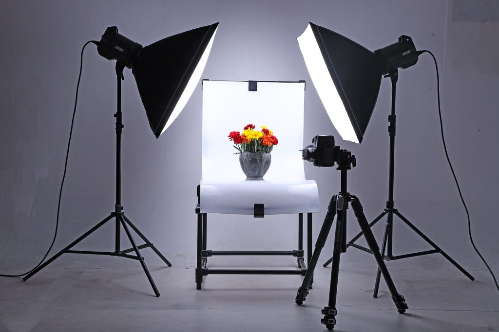 Tabletop product photography setup with softbox lights and a camera aimed at a flower arrangement, illustrating shooting real inventory rather than generating it