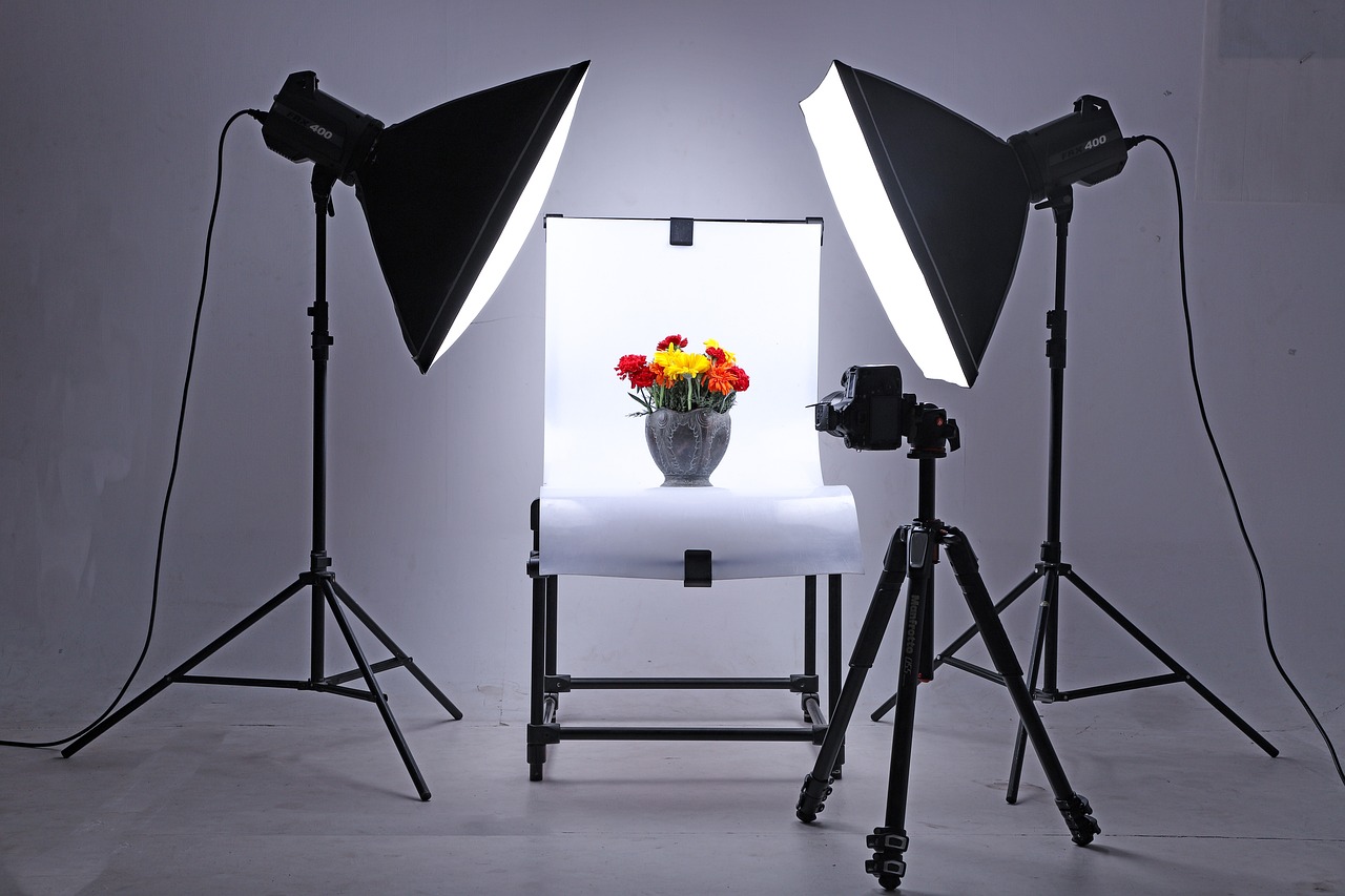 Tabletop product photography setup with softbox lights and a camera aimed at a flower arrangement, illustrating shooting real inventory rather than generating it