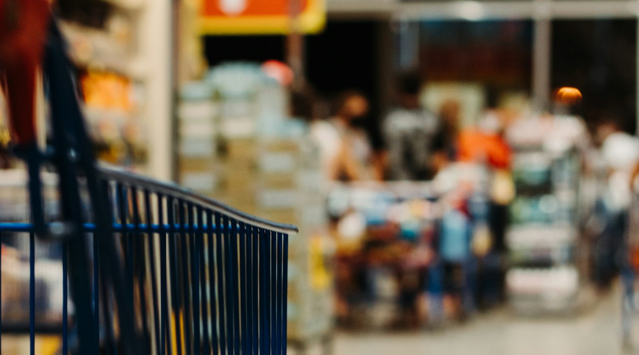 Shopping cart in a retail store aisle with a blurred checkout area beyond, illustrating paid traffic sent to a retailer site rather than a brand own store
