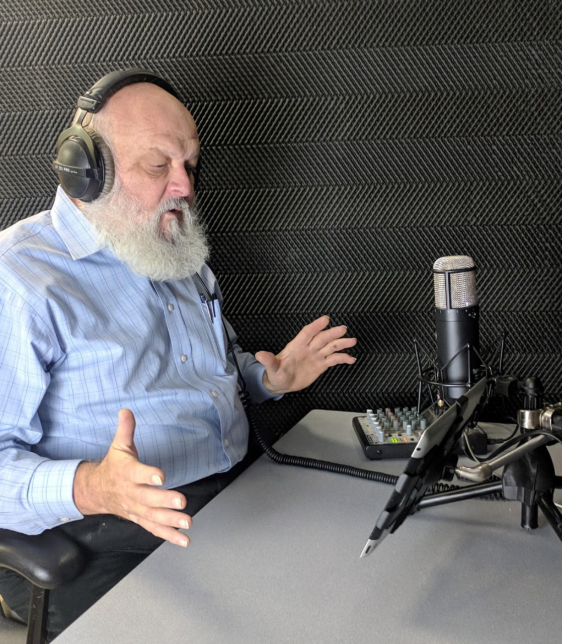 Voice-over artist wearing headphones speaking into a condenser microphone in a soundproofed booth, the recording step AI ad dubbing now replaces