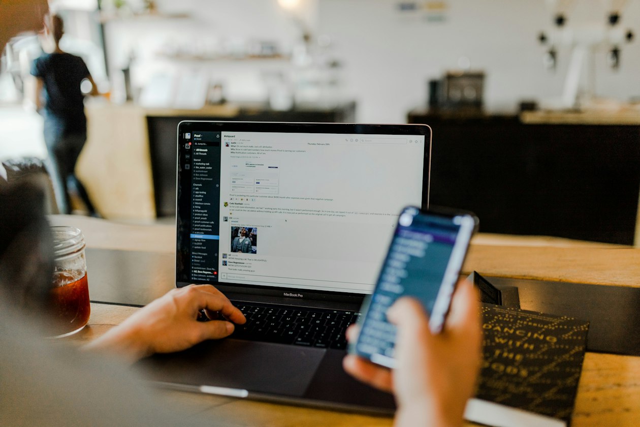 Person scrolling a social feed on a smartphone beside an open laptop in a cafe, illustrating a small team weighing Threads ads