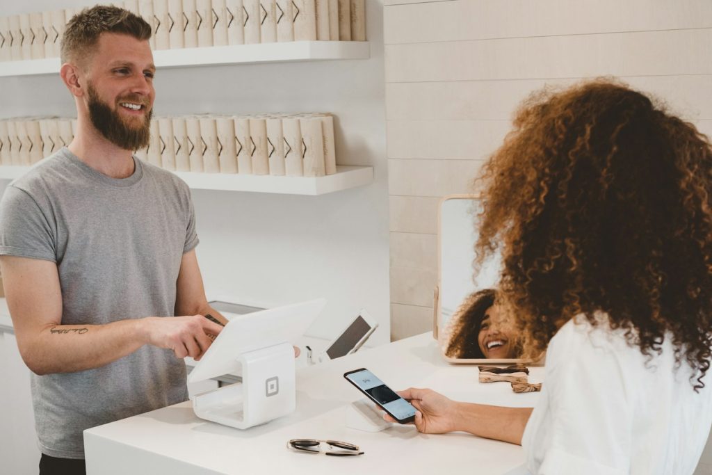 Customer paying with a smartphone at a bright boutique checkout counter, illustrating the checkout step Google now handles inside AI Mode and Gemini