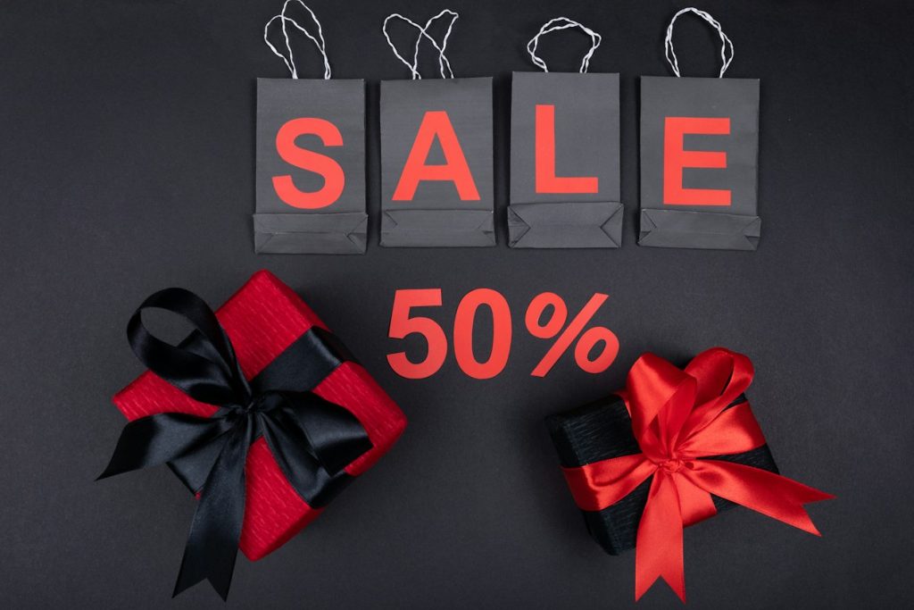Black shopping bags spelling SALE in red letters above a red 50% sign and two wrapped gifts, illustrating a Black Friday promotion window