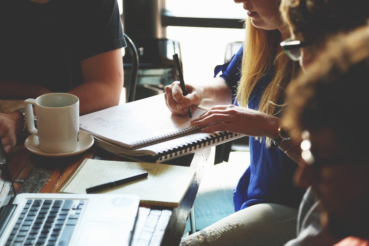 Small team taking handwritten notes around a café table with a laptop and coffee, illustrating a B2B team reviewing lead quality against pipeline
