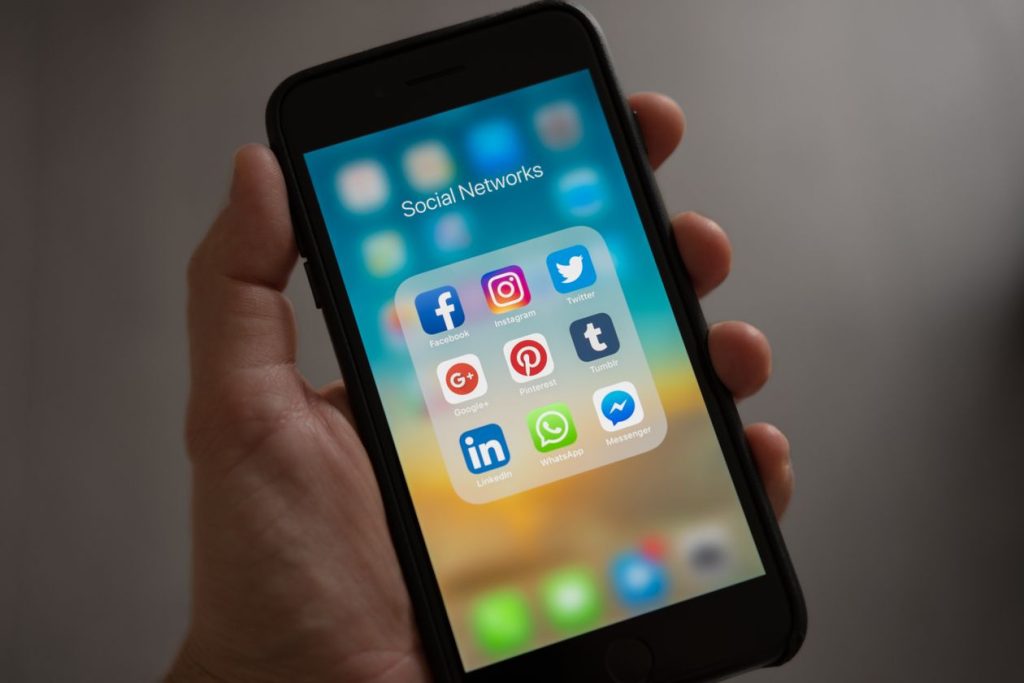 Hand holding a smartphone open to a Social Networks app folder, illustrating lead capture moving off Reddit's native forms onto an advertiser's own page