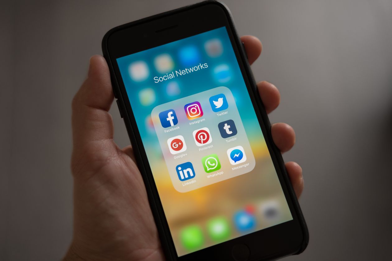 Hand holding a smartphone open to a Social Networks app folder, illustrating lead capture moving off Reddit's native forms onto an advertiser's own page