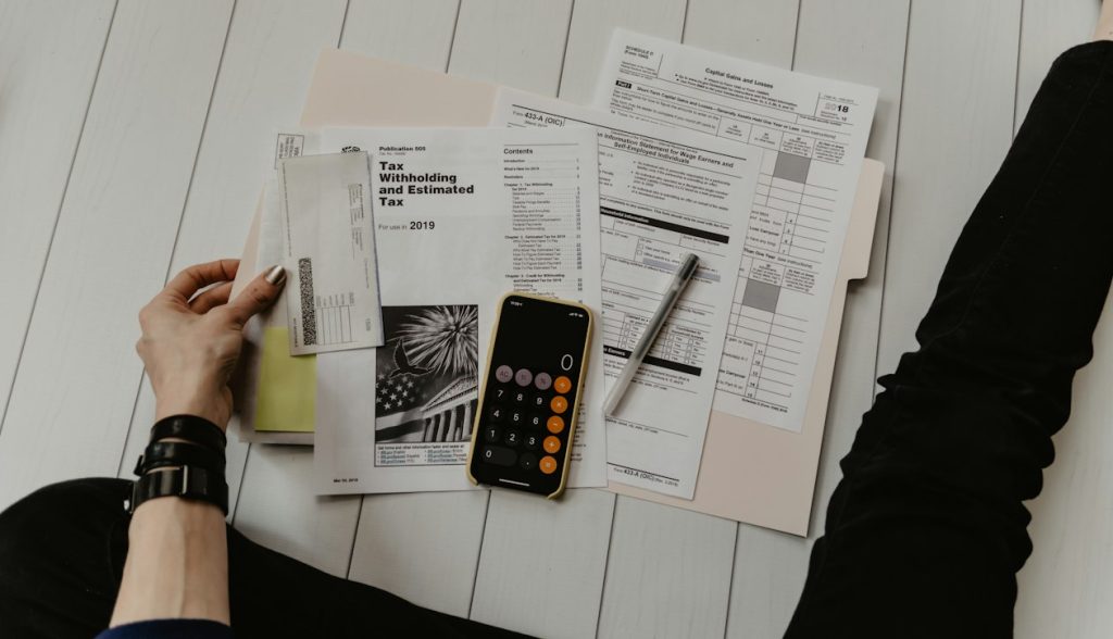 Person sorting printed tax forms and receipts beside a phone calculator and pen, illustrating a small firm reviewing how its fixed ad budget is split