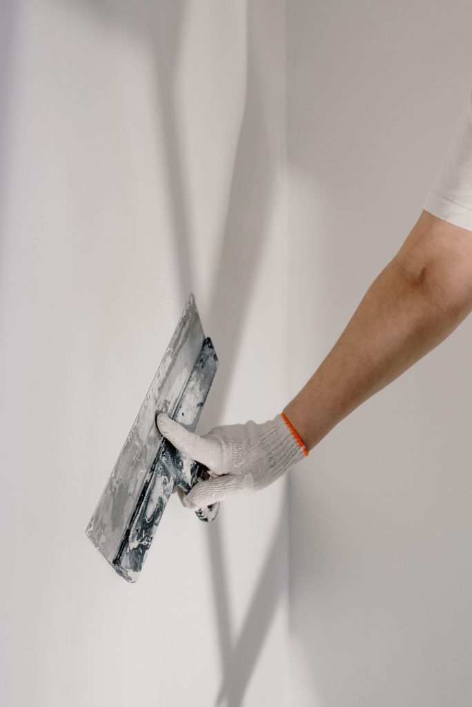Contractor in a work glove smoothing plaster on a wall with a trowel, representing a home-improvement business answering ad leads between jobs
