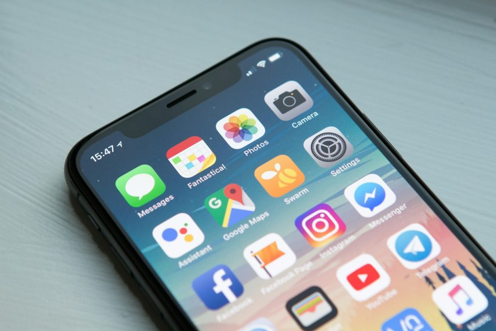 Smartphone home screen filled with app icons on a light table, illustrating TikTok ads now running inside third-party apps beyond TikTok
