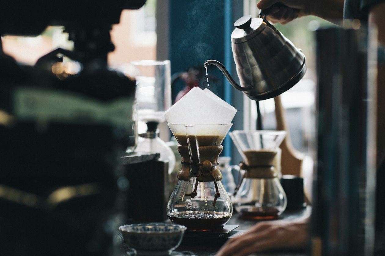 Barista pouring water from a gooseneck kettle into a pour-over coffee brewer, illustrating a small coffee brand deciding who its first-order ads should reach