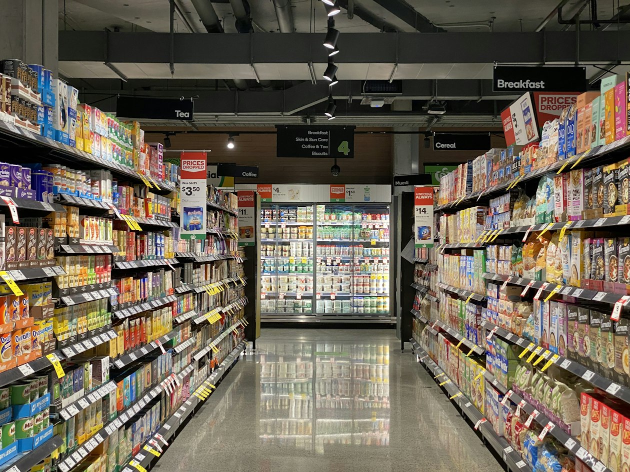 Brightly lit grocery aisle lined with stocked shelves and price labels, illustrating how frequently changing shelf and feed prices trigger Merchant Center disapprovals