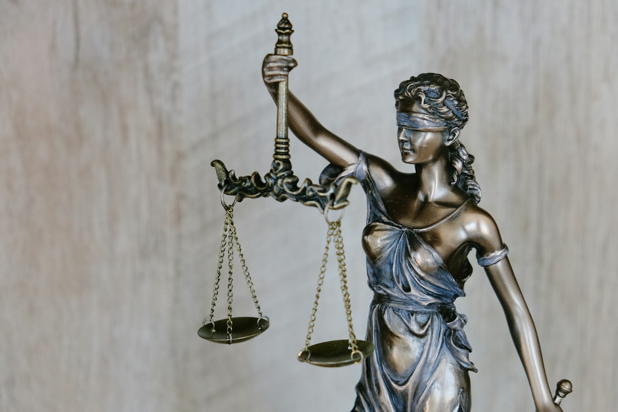 Bronze statue of blindfolded Lady Justice holding scales against a pale wall, illustrating Meta's updated advertising terms and advertiser liability