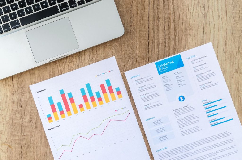 Printed reports with bar and line charts beside a laptop on a wooden desk, illustrating a conversion-tracking audit for a small Google Ads account